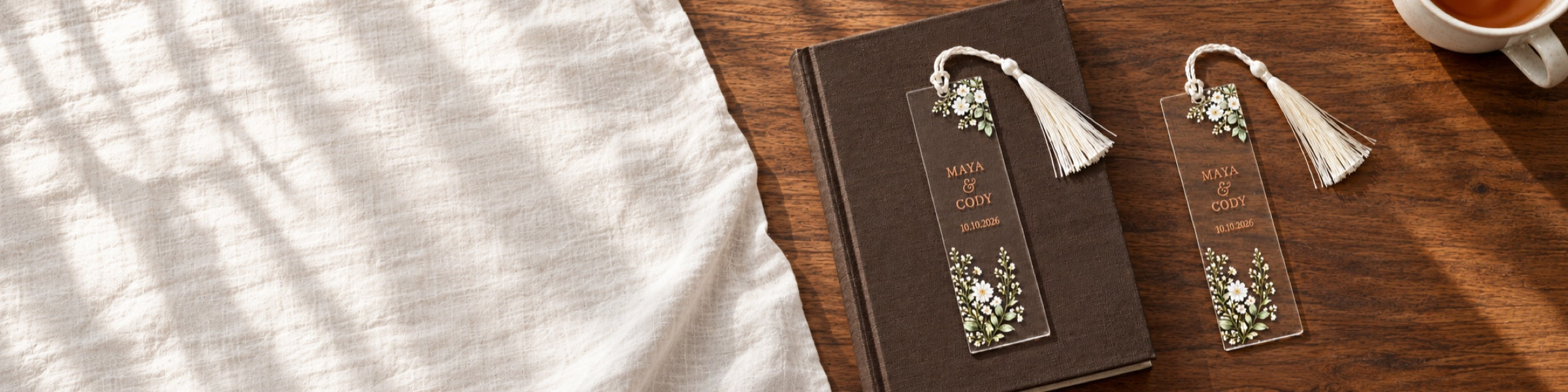 Two personalized clear acrylic floral bookmarks with ivory tassels on an espresso clothbound book and walnut reading table