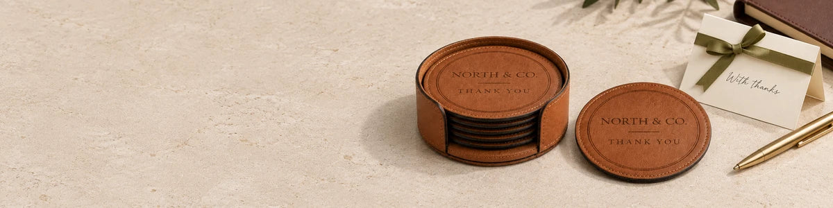 Personalized tan North and Co. leatherette coasters and matching holder beside a thank-you card on a pale stone surface