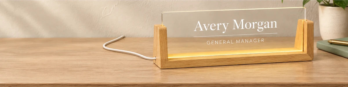 Illuminated Avery Morgan General Manager acrylic nameplate in a natural wood base beside a sage notebook and ivory potted plant